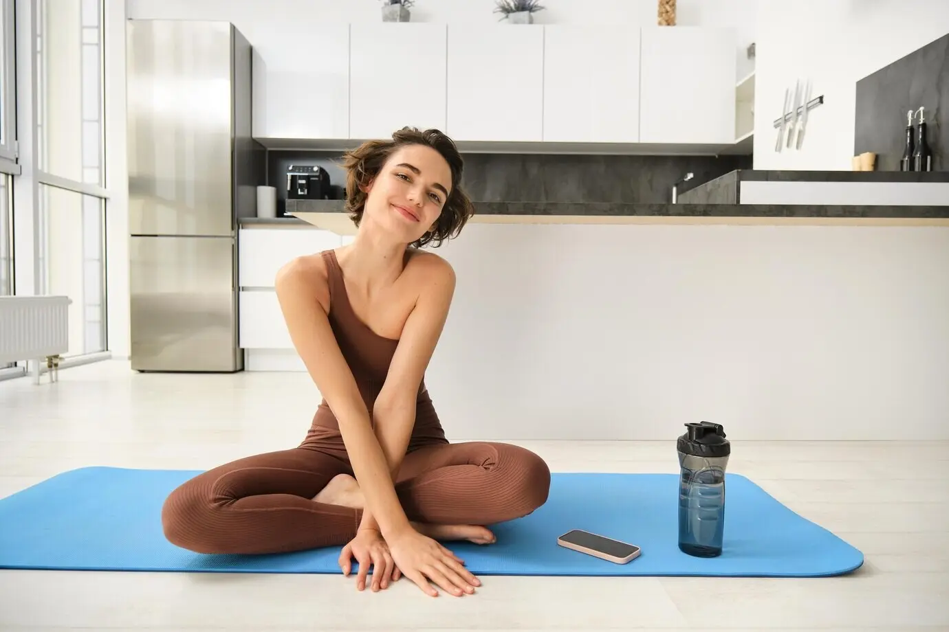Porträt eines Fitness-Girls, das beim Heimtraining drinnen in der Küche auf einer Gummimatte Yoga macht und Sportbekleidung trägt.